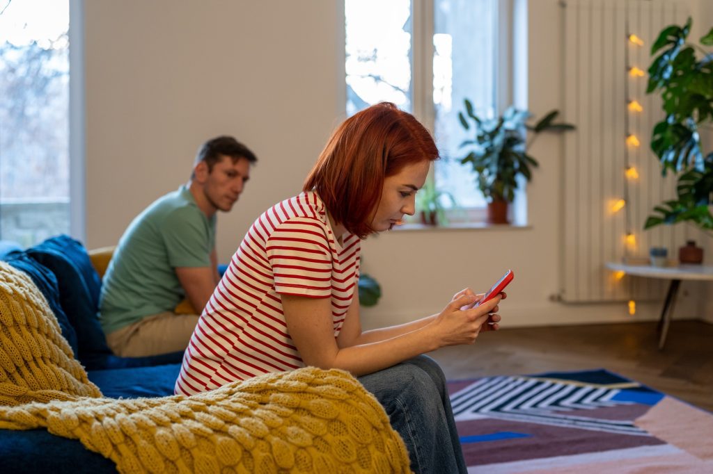 Toxic relationship. Couple sits on couch after quarrel. Girl writes support from domestic violence